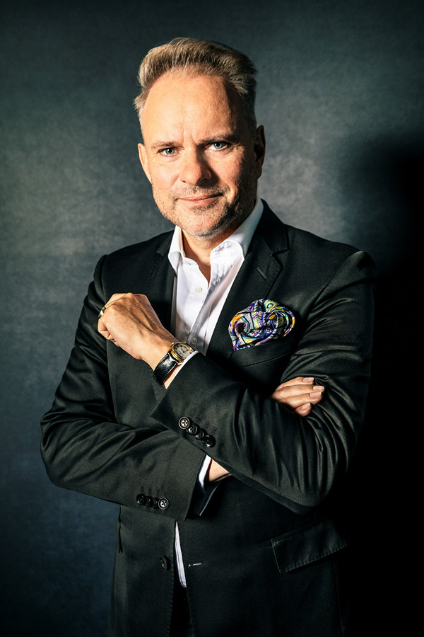 Tobias Bringmann in dunklem Anzug mit gepunkteter Einstecktuch, Armbanduhr und verschr&auml;nkten Armen.