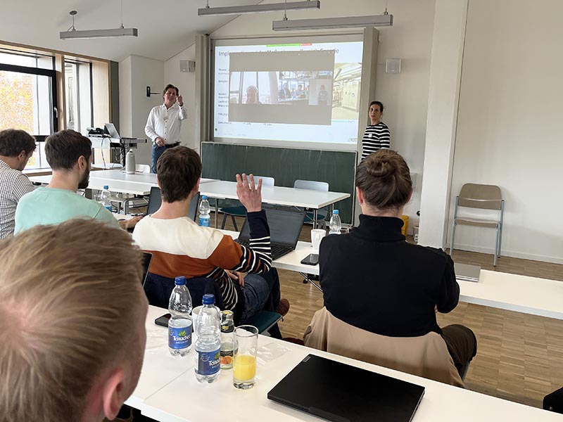 Personen im Seminarraum mit Frontvortrag.