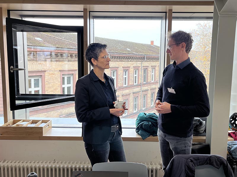 Zwei Personen in Businesskleidung unterhalten sich am Fenster.