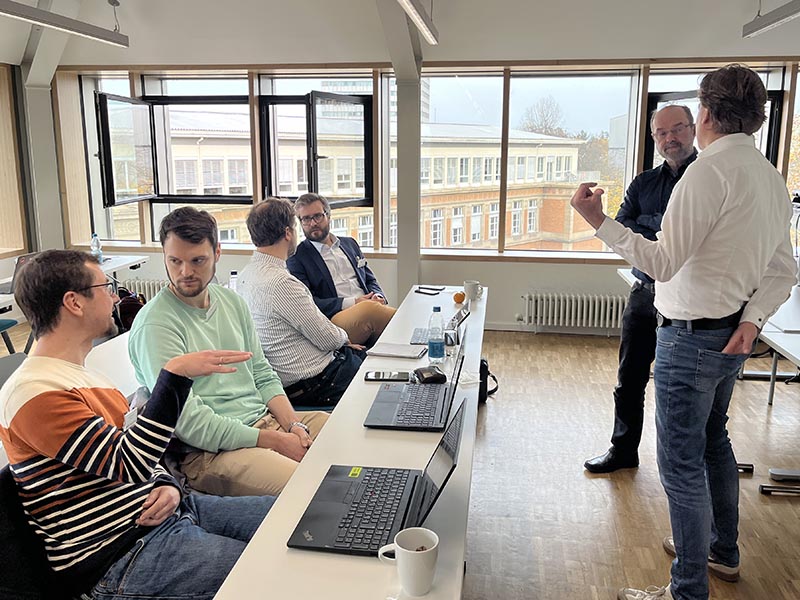 Gruppe von Menschen in Konferenzraum mit geöffneten Fenstern.
