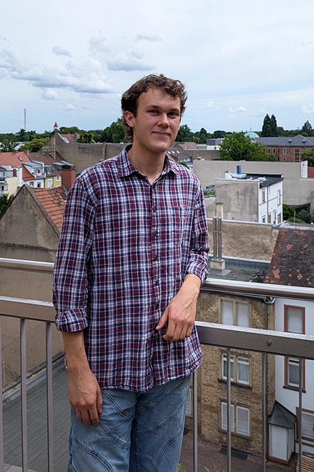 Yannic Flad steht auf einem Balkon vor der Stadtkulisse Karlsruhes.